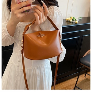 Brown leather bucket bag with gold twist lock held by model in indoor setting