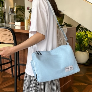 Sac bandoulière en toile bleu clair minimaliste porté par un mannequin en décor cosy