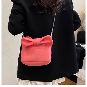 Détail d'un sac à bandoulière rose avec nœud et chaîne argentée porté par un mannequin