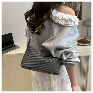 Detail of woven hobo bag with gold chain strap worn by a model in a minimalist setting