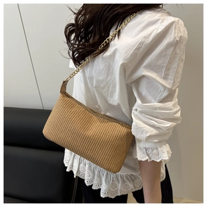 Close-up of handmade woven straw crossbody bag with golden chain strap for summer travel