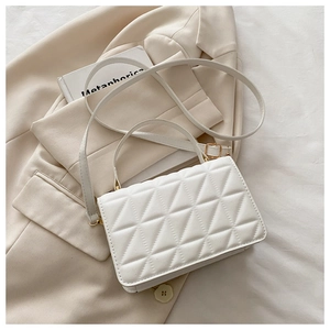 Detail of white quilted crossbody bag with gold hardware on a beige blazer background