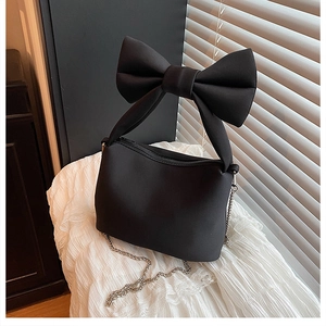Detail of black bow handbag featuring oversized fabric handle and delicate metal chain strap