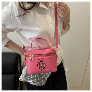 Sac boîte rose en cuir grainé avec logo M doré porté à l'épaule par un mannequin