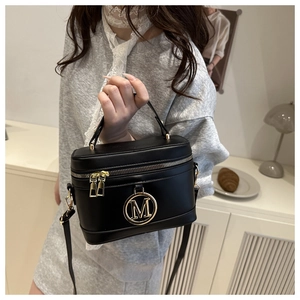 Dettaglio di una borsa a scatola nera strutturata con logo M dorato e tracolla regolabile