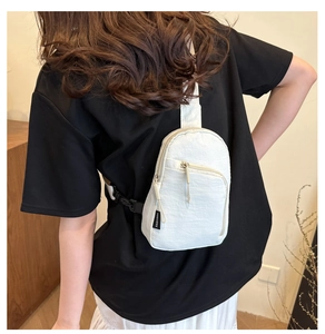 Détail du sac de poitrine en nylon blanc montrant les zips et l'étiquette tissée