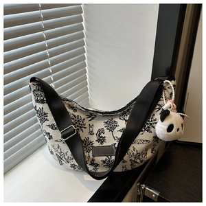 Close-up of crescent canvas tote bag with hand-drawn tree prints and panda plush charm