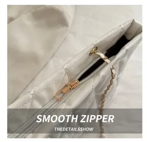 Detail of light gold zipper and chain strap on a white quilted leather tote bag