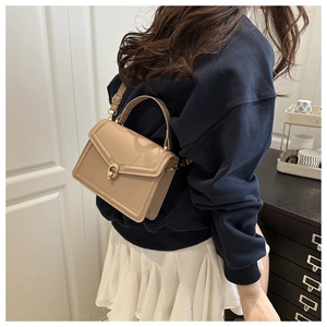 Femme portant un petit sac carré beige avec un fermoir rotatif doré dans un cadre épuré