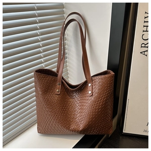 Close-up of brown woven tote bag featuring dual handles and metallic rivet details