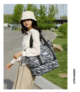 Outdoor shot of a large zebra print travel tote with black straps and brand label