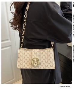 Détail du sac beige à motif monogramme avec un fermoir à boucle en métal doré en forme de M
