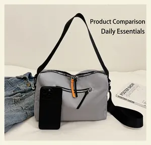 Close-up of grey nylon crossbody bag with orange zipper pull and iPhone size reference