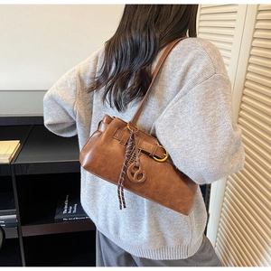 Detailed close-up of brown faux leather shoulder bag with gold hardware and woven pendant