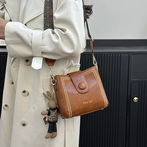 Brown bucket bag with gold studs, ethnic strap and rabbit charm on model