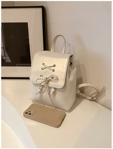 Mini-Rucksack aus cremefarbenem Kunstleder mit Schleife, gezeigt neben einem Smartphone