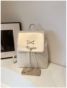 Detail eines cremeweißen Kunstleder-Rucksacks mit dekorativer Schleife und Perlmutt-Finish