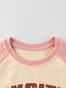 Dettaglio del colletto a costine rosa e maniche raglan su t-shirt crema per bambini