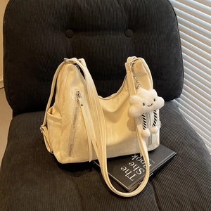 Chic cream marble texture shoulder bag with plush charm on dark corduroy chair