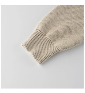 Detailed macro view of the beige knitted sweater's ribbed cuffs and high-quality texture