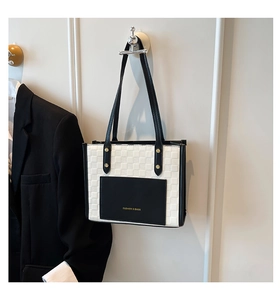 Detail of checkered tote bag featuring a black leather pocket with gold fashion logo