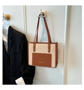 Detail of checkered patchwork shoulder bag with front leather pocket and logo hanging on wall
