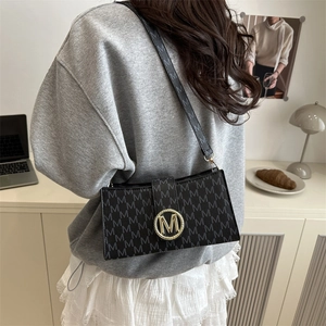 Sac à aisselle noir minimaliste avec motif M gris et boucle dorée avec logo