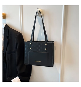 Detail of black leather tote bag with checkered texture, gold rivet accents and front pocket