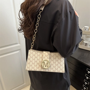 Sac bandoulière beige chic avec motif M et chaîne dorée porté par un mannequin