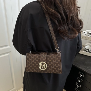Sac bandoulière marron rétro à monogramme avec boucle dorée porté par un modèle