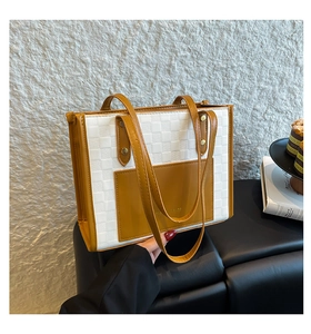 Detail of checkered square tote bag with brown leather handles and front pocket design