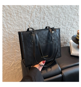 Detail of black leather tote bag featuring woven texture and gold lettering on front pocket