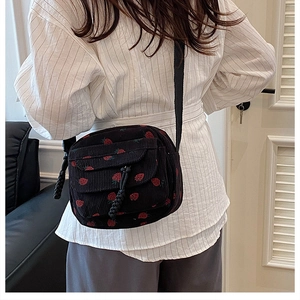 Close-up of black corduroy crossbody bag with cute strawberry pattern and woven pendants