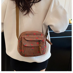 Brown corduroy crossbody bag with red strawberry prints worn by a model in a casual outfit