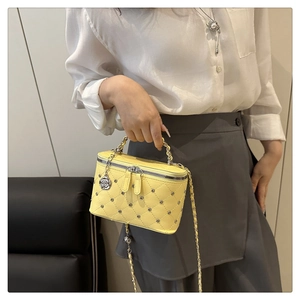 Close-up of yellow quilted chain bag with silver studs and floral charm detail