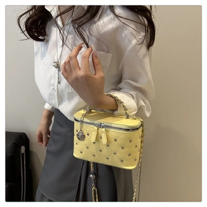 Detail view of a yellow quilted mini crossbody bag with silver studs and rose pendant