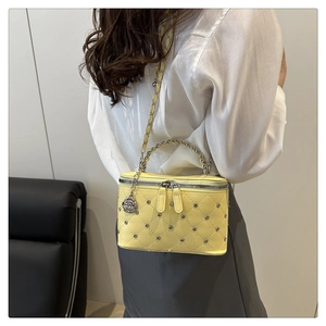 Detail of yellow quilted box bag with silver studs and rose-shaped metal pendant charm