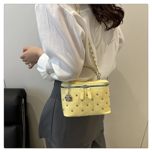 Detail of lemon yellow quilted leather box bag with studs and chain strap shown on shoulder