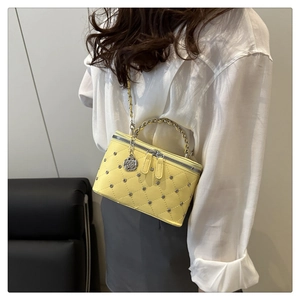 Detail view of yellow quilted vanity bag with silver rivets and metallic chain handle