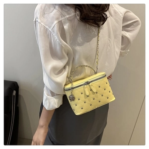 Detail of yellow quilted box bag with metal beads and rose charm on a chain strap