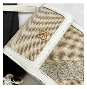 Detail of canvas crossbody bag with white leather trim and gold clover metal clasp