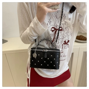 Detail view of black quilted box bag with silver studs and rose charm on crossbody strap