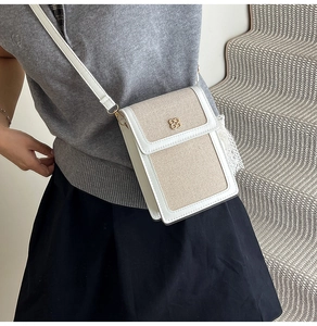Close-up of beige woven crossbody bag with white leather trim and gold clover buckle detail