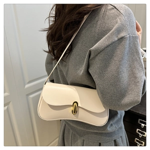 On-shoulder view of a creamy white leather baguette bag with wavy flap and gold buckle