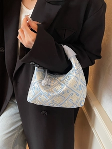 Blue embroidered handbag with traditional patterns held by model in black blazer