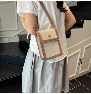 Detail of beige canvas crossbody bag with brown leather trim and gold clover clasp on model
