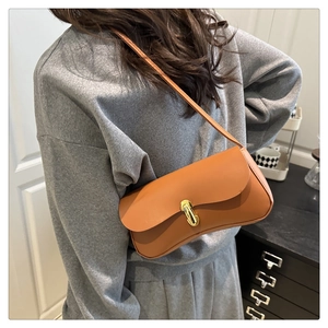 Brown leather underarm bag featuring a metallic cylinder clasp shown on a model