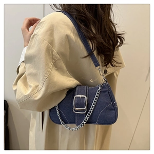 Detail of blue denim shoulder bag with silver buckle and chain on beige trench coat
