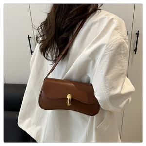 Brown minimalist shoulder bag with gold cylinder clasp shown on model in home setting