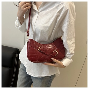 Detail of burgundy underarm bag with crocodile texture and golden metal buckles